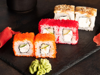 Sushi rolls and sashimi in a black stone plate. Traditional Japanese cuisine with salmon, fish, wasabi, soy sauce, and ginger. Chopsticks and two cups of traditional sake