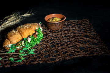 Fresh croissant sandwich with lettuce and prosciutto on dark background. Delicious and healthy breakfast