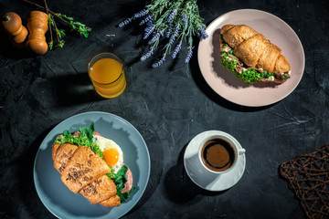 Fresh croissants sandwiches with lettuce, fried egg, prosciutto and cup of coffee on dark background. Delicious and healthy breakfast