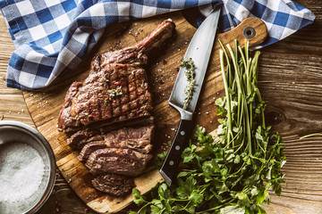 Freshly grilled tomahawk steak on slate plate with salt pepper rosemary and parsley herbs. Sliced...
