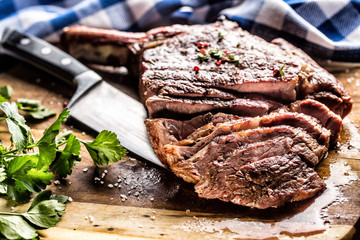 Freshly grilled tomahawk steak on slate plate with salt pepper rosemary and parsley herbs. Sliced pieces of juicy beef steak