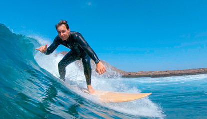 CLOSE UP: Happy male surfer riding a wave and giving the camera the shaka sign.