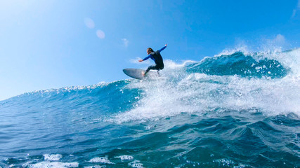 LOW ANGLE, LENS FLARE: Cheerful surfer riding big ocean wave in sunny nature.