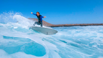 LOW ANGLE: Surfer guy carves a wave and splashes water at the camera. © helivideo