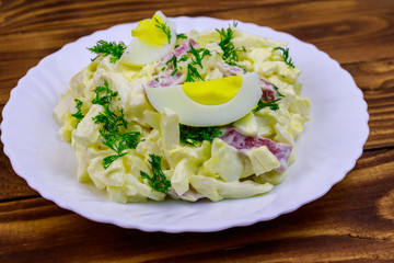 Salad with chinese cabbage, onion, sausage, eggs and mayonnaise on wooden table
