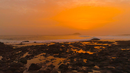 Foaming water coming from the ocean cleansing the rocky black beach at sunset.