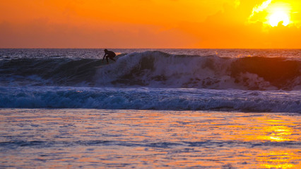 Cool tourist on surfboard carving dangerous deep blue breaking wave at sunrise.