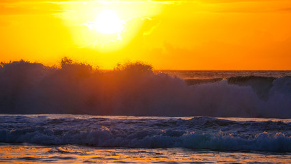 Fototapeta na wymiar Golden evening sunbeams shine on the big barrel wave rolling towards the shore.