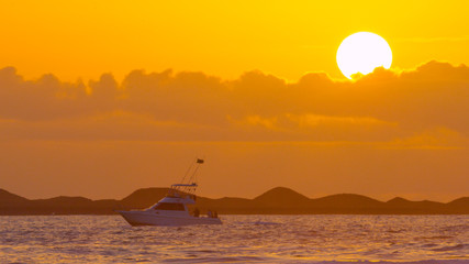 Lone small boat slowly drifting through peaceful ocean on at breathtaking sunset