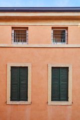 Fototapeta na wymiar Building's facade. Two antique windows with closed shutters and two plastic windows.