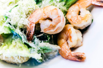 Caesar salad with shrimps on white plate in restaurant.