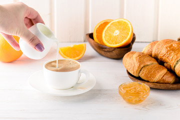 Coffee white cup, croissants on white background, selective focus. female hand pours cream into coffee