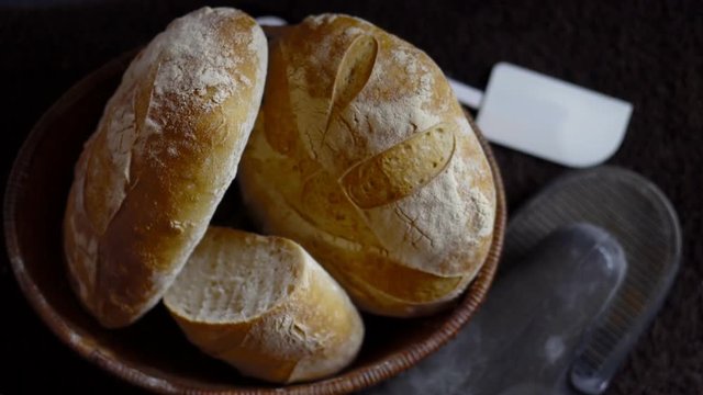 a slow zooming shot of a basket of crusty sourdough boule and batard with baking gloves and spatula