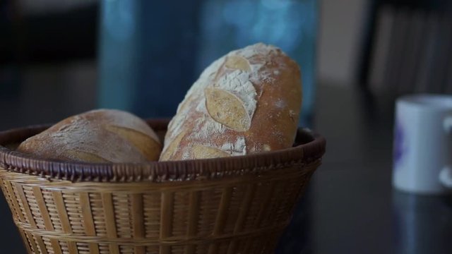 Crusty, golden brown sourdough bread in a basket with a coffee cup on a dark table