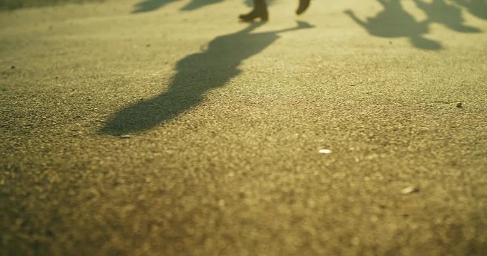 Walking man on asphalt in early morning sun creating nice and long shadows in slow motion.