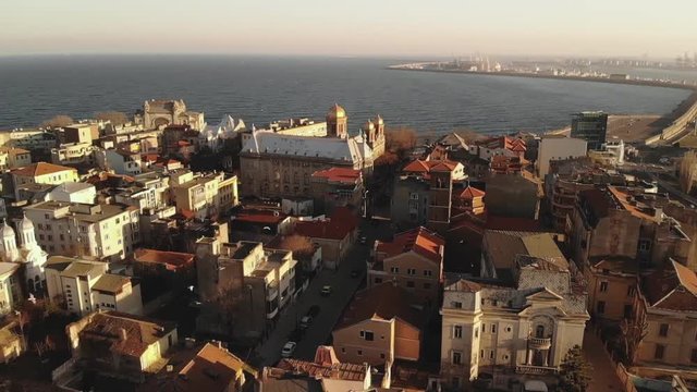 Pan aerial shot of Old Town Constanta City and harbor, Romania, Europe. Shot in spring during sunset and Golden Hour, revealing the Black Sea, harbor and the architecture while seagulls fly