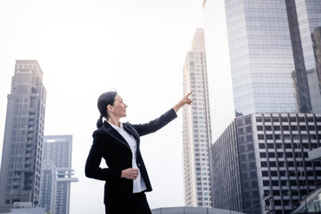 Fototapeta na wymiar Successful senior businesswoman leader pointing and looking forward over modern building background