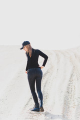 Woman wear black turtleneck, jeans and baseball cap, girl in sand desert. Fashionable casual style, fashion and clothes concept of modern look