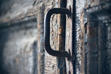 Rusty metal handle on an old wooden door with crumbling paint, which most likely leads to the...