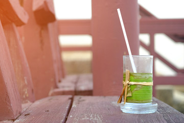 Water glass with green banana leaf wrapped around, and the straw, and saucer, on wooden chair