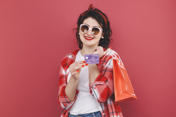 Portrait of happy nice girl with curly hair holding bags and credit card after shopping isolated over the yellow background