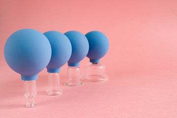 four blue cosmetic vacuum jars of different sizes made of glass and rubber on pink background
