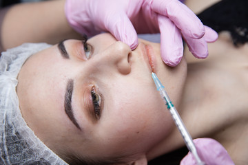 Obraz na płótnie Canvas The doctor cosmetologist makes the Rejuvenating facial injections procedure for tightening and smoothing wrinkles on the face skin of a beautiful, young woman in a beauty salon.