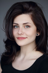 Obraz premium Cute brunette girl with beautiful green eyes,wavy hair with volume looks at camera and smiles sweetly and innocent.