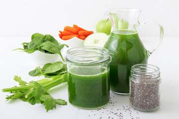 Fototapeta na wymiar Vegetable smoothie, healthy organic juice made from celery, green apples, leaves of spinach and young carrot. Big pitcher and jar of green juice, small jar with chia seeds. Prevention of diabetes.