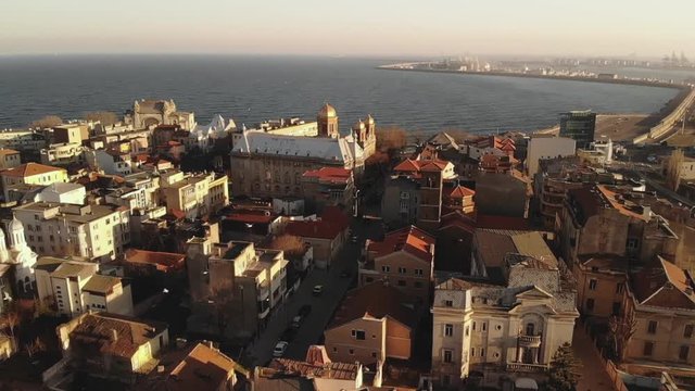 Pan aerial shot of Old Town Constanta City and harbor, Romania, Europe. Shot in spring during sunset and Golden Hour, revealing architecture and boats while seagulls fly