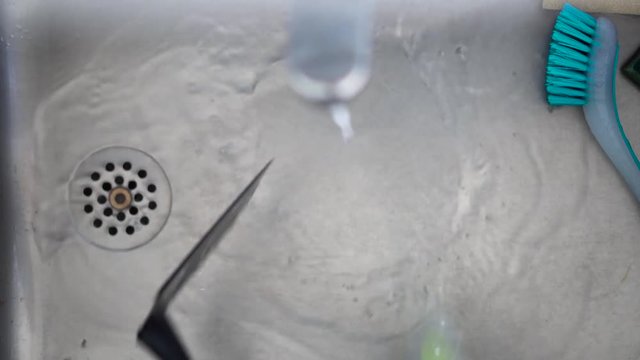 Black plastic spatula is cleaned with a long green brush in a grey sink with a blue brush right next to it