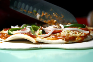 Ham, pepperoni, cheese with green bell pepper pizza being sliced