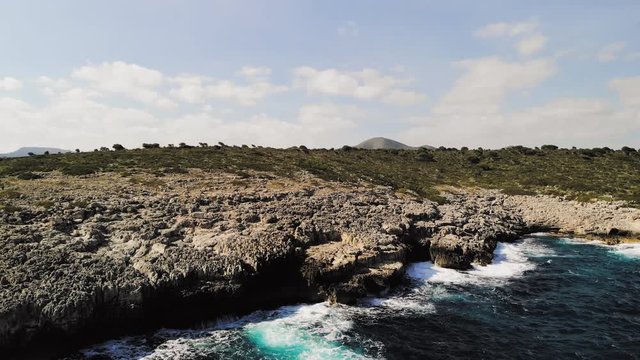 a drone shot rotating to show waves splashing onto a rocky shore and spraying into the air near cala varques in majorca