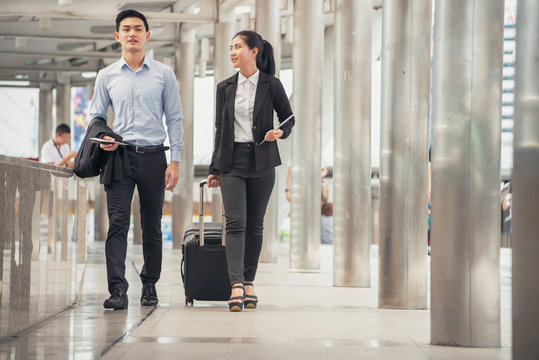 Business man and woman  Dragging suitcase luggage bag,walking to passenger boarding in Airport,travel to work.Asian tourist men and women  wearing black suit pull trolley bag. Business travel concept
