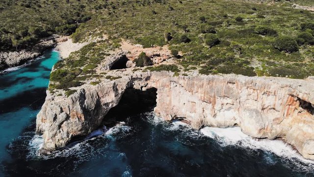 a wide drone shot flying forward towards a large sea arch near cala varques in majorca