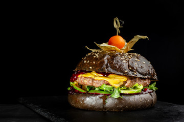 Fresh tasty burger on black slate, decorated with Physalis.