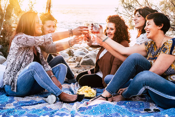Group of happy cheerful young women enjoy and celebrate the friendship toasting with wine glasses and smiling together - sunny light in background for friendship concept in outdoor beach
