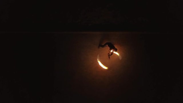Aerial: Young blond male does tricks with fire, spins two burning torches