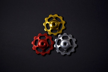 Color rollers, black, golden, silver gears for bicycle rear derailleur on black color in shape of triangle with shadow