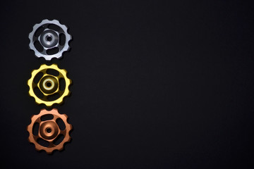 Color rollers, silver, golden, copper gears for bicycle rear derailleur on black background in left side, with copyspace