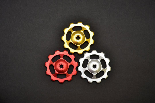 Color rollers, black, golden, silver gears for bicycle rear derailleur on gray background in shape of triangle © Mykola
