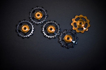 Color rollers, black, golden gears for bicycle rear derailleur on black background with copyspace