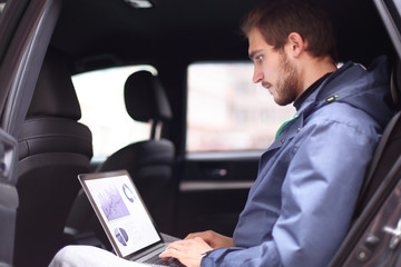 handsome businessman sitting in luxury limousine, working on laptop computer