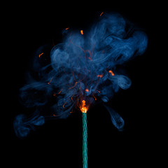Burning dynamite fuse with sparks and smoke on black background.