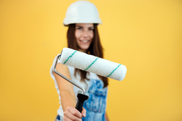 Closeup of happy beautiful young woman in construction uniform and protective helmet shows you paint roller