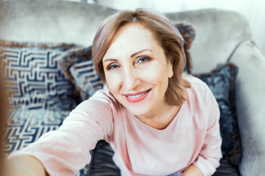 Elderly Woman With a Phone in Her Hands in Good Mood is Resting at Home in the Living Room.