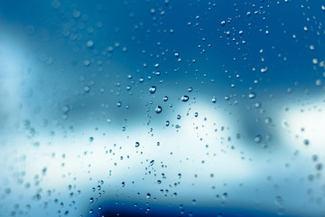 Water drops on the window, blue sky and clouds in the blurry background.