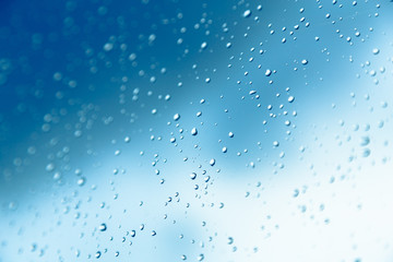 Water drops on the window, blue sky and clouds in the blurry background.