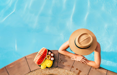 Woman in straw hat in pool with plate og tropical fruits