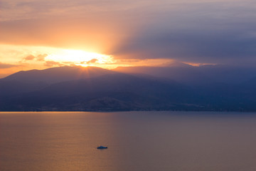 beautiful dramatic north scenery landscape with sunset and rays from mountain ridge silhouette above calm lake water surface and small yacht, daily planet travel photography